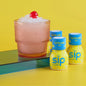 Cocktail with a cherry and ice next to Sip Elixirs bottles on a colorful background