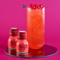 Red cocktail with cherries and 'sip Elixirs' bottles on a pink background
