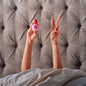 Person lying in bed holding a pink bottle with 'sip' branding, making a peace sign.